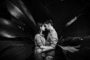 a couple holding each other in front of huge plant