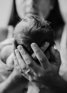 Hände einer Mutter halten den Kopf ihres neugeborenen Babys