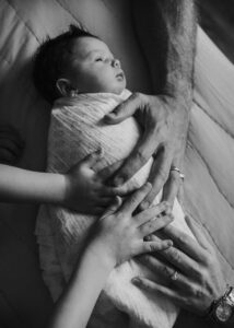 Hände von Eltern und Geschwistern auf Bauch des neugeborenen Babys