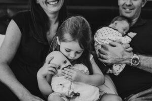 Eltern mit neugeborenem Baby und Schwester mit Babypuppe