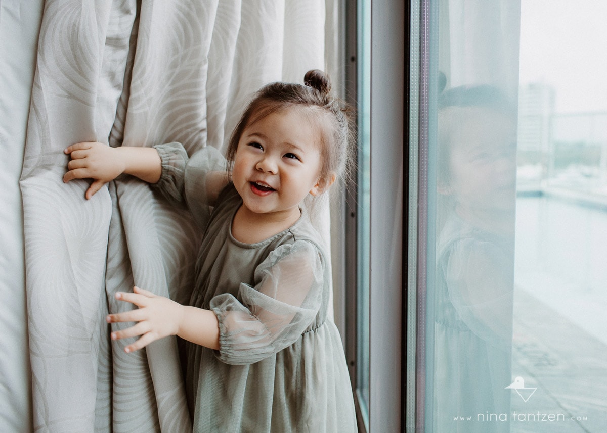girl playing with curtain by window